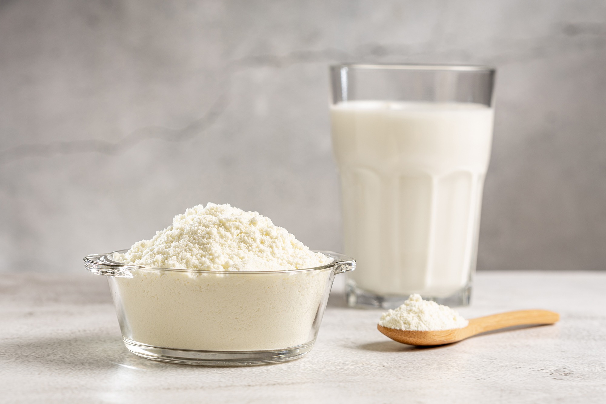 Milk powder in a glass bowl beside a glass of milk