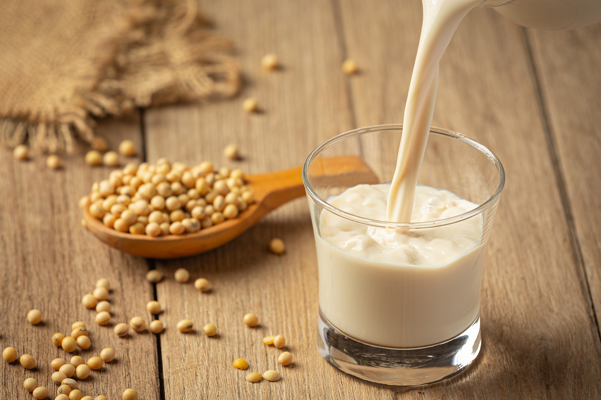 Soya milk being poured into a glass beside soybeans